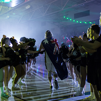 Athletes enter the gym surrounded by cheer leaders and team members